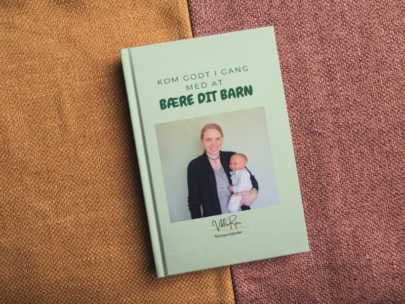 Guiden "Kom i gang med at bære dit barn" vist som bog liggende på gult og rødt stof
